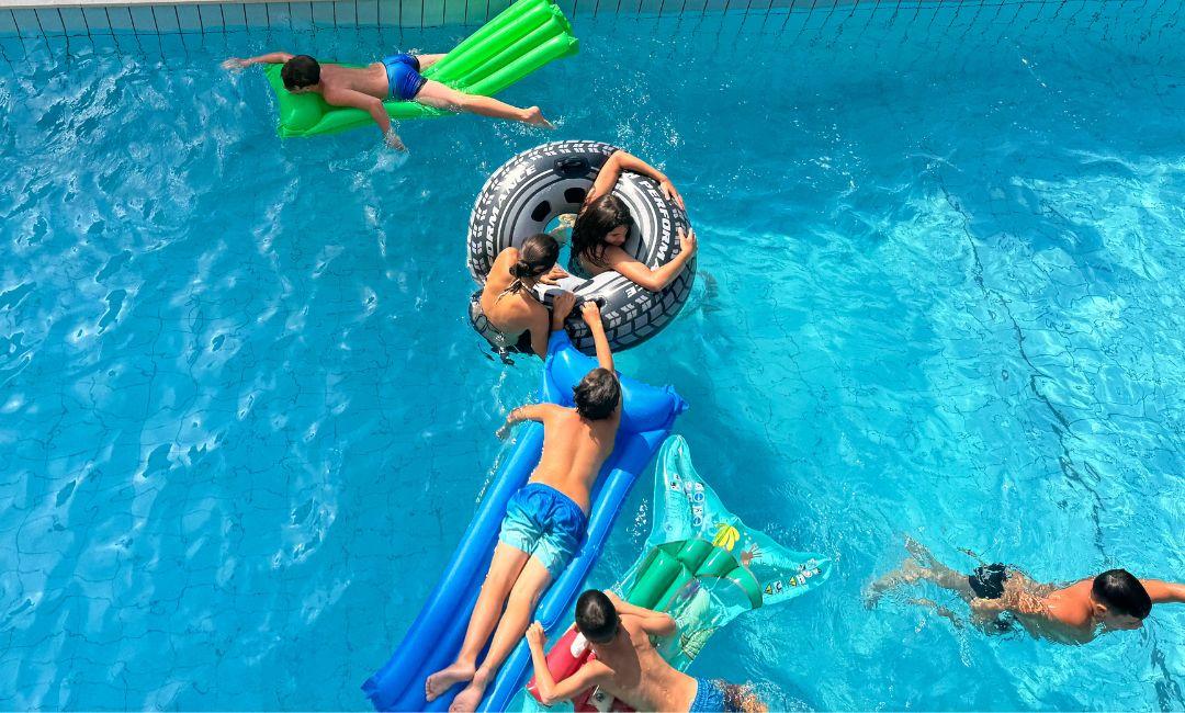 Bambini giocano in piscina con materassini gonfiabili colorati.