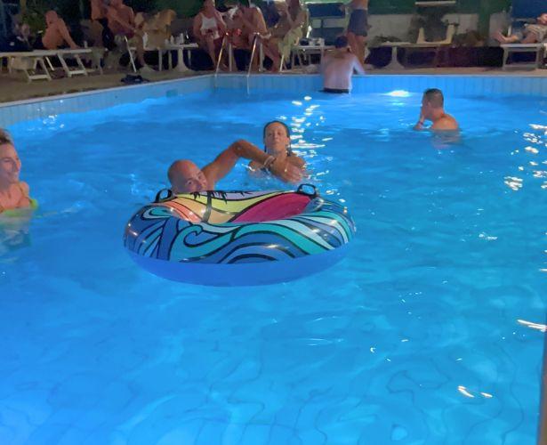 Persone in piscina di notte, con un grande salvagente colorato.